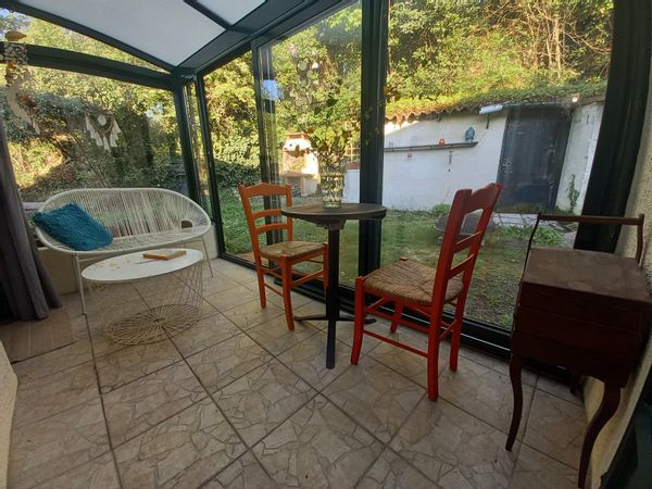 Petite maison avec véranda, entourée de verdure.
