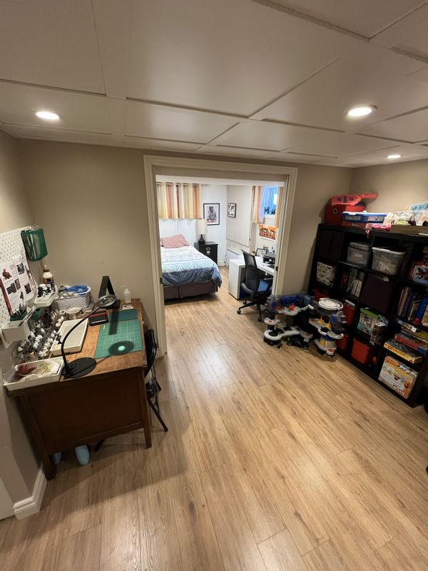 Espace bachelor au sous-sol avec chambre fermée, une salle de bain avec douche, frigo et salon.